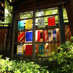 In the front yard of Helen Rosenau’s Eugene home hang several of her fused-glass artworks. Rosenau, who prefers to work in square, says this piece, Her Twelve Tribes, represents “the world of the unseen.” (Photography by Collin Andrew/The Register-Guard)